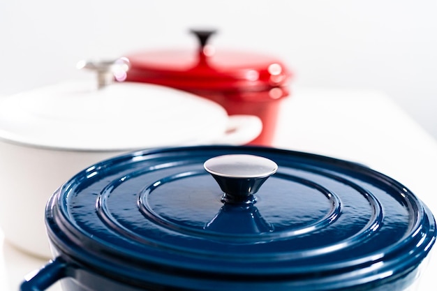 Fornos holandeses redondos cobertos de ferro fundido esmaltado vermelho, branco e azul em um fundo branco.